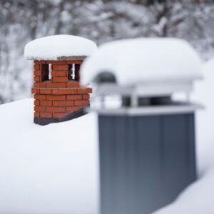two chimneys with snow on top, one being masonry and one being gray and prefabricated