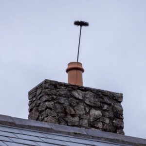 a chimney sweep brush stick out of the top of a masonry chimney