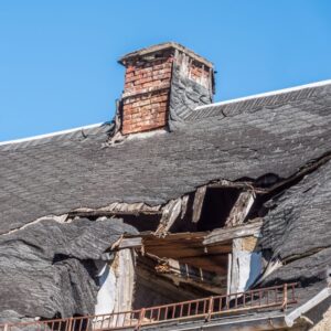 a damaged masonry chimney on a roof with a big hole in it