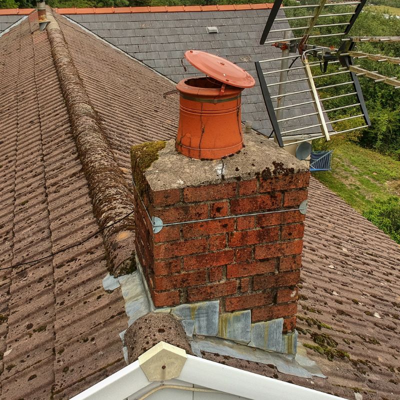 a masonry chimney with rusted flashing a broken chimney pot, and crumbling bricks
