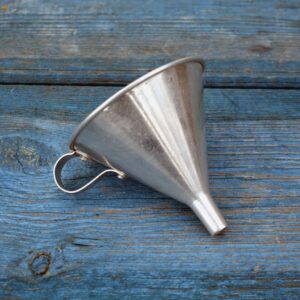 a gray metal funnel with a little handle laying on a wood surface