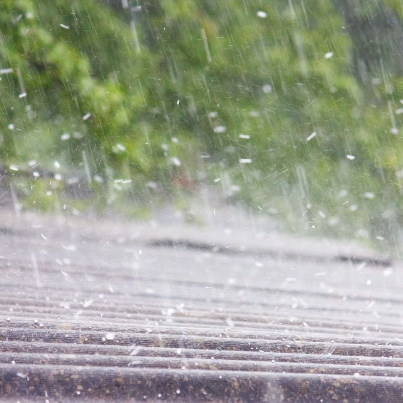 rain coming down on a brown roof with trees in the background