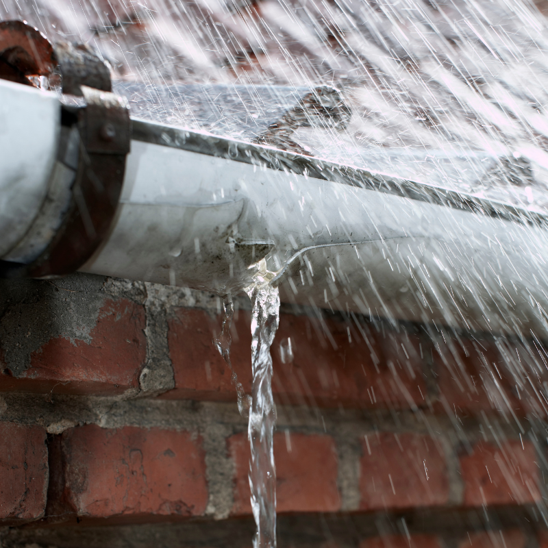 rain falling off a roof and gutter with a brick wall in the background