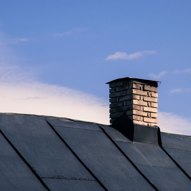 a masonry chimney on a black roof with a blue sky in the background