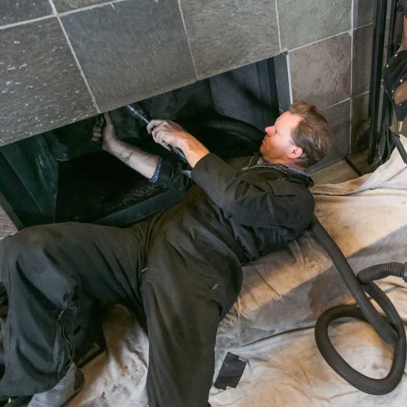 stock photo of chimney sweep a man by a fireplace opening using a chimney sweep vacuum to clean the flue